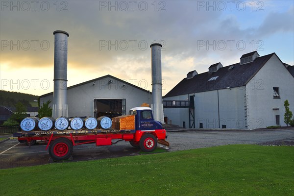 Old lorry loaded with whiskey barrels parked in front of a distillery