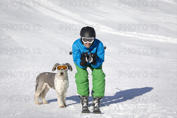 A skier and his dog with snow goggles on a ski slope