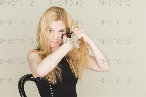 Teenage girl cutting her hair with scissors