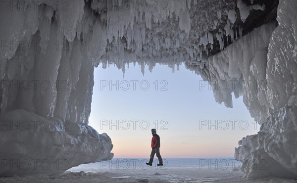 Ice formations and icicles hanging from ceiling in a cave and a man walking on frozen Lake Superior