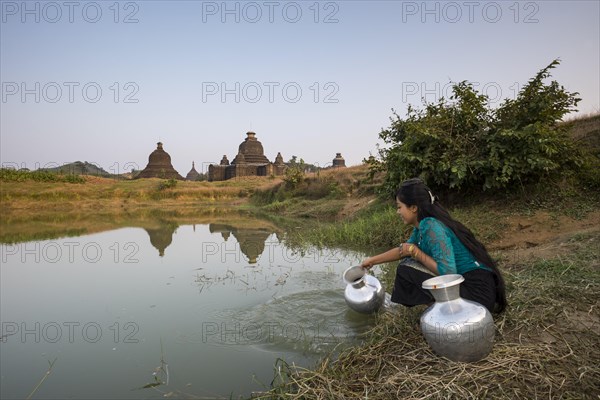 Smiling girl drawing water from a water hole with a vessel made of aluminium