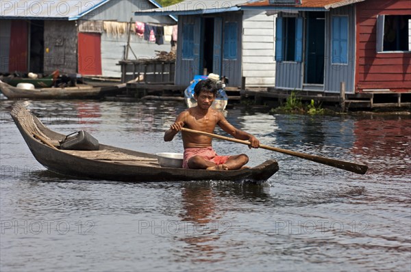 Man paddling a boat near a floating village on Tonle Sap Lake