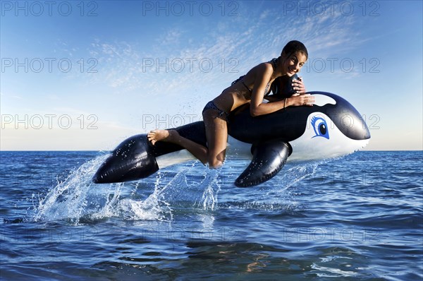 Girl sitting on an inflatable orca jumping out of the water