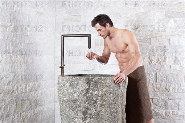 Bare-chested man standing at a water fountain in a spa complex