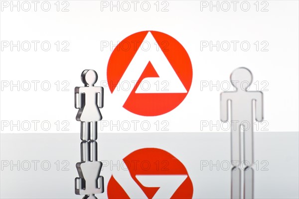 Two figures standing in front of the logo of the German employment agency