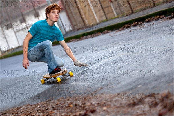 Teenager riding a longboard downhill on a wet street