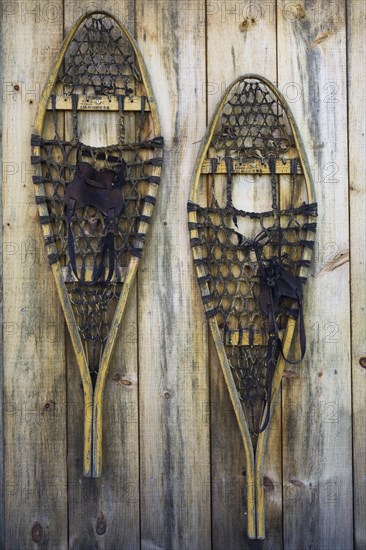 A pair of old wooden snowshoes hanging on the pine board wall of a storage shed