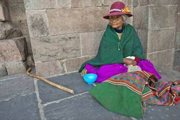 An elderly woman in traditional dress of the Quechua Indians sitting on the floor in front of an Inca wall