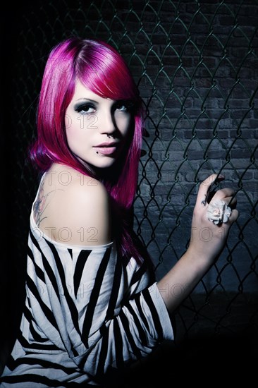 Woman with pink hair in front of a chain link fence