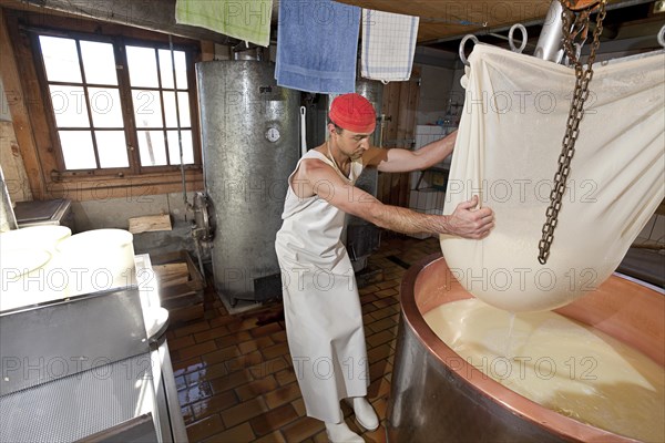 Dairyman raising the cloth with cottage cheese from the copper kettle to drain off the whey