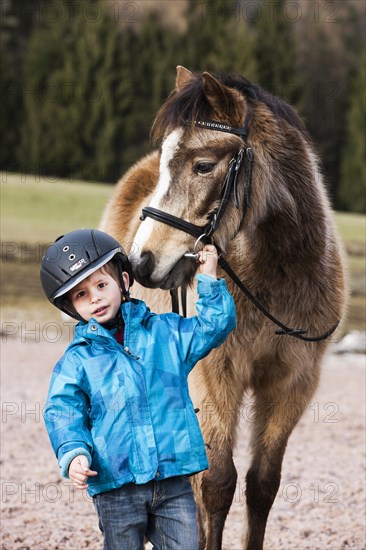 Young child wearing a riding helmet standing beside a pony