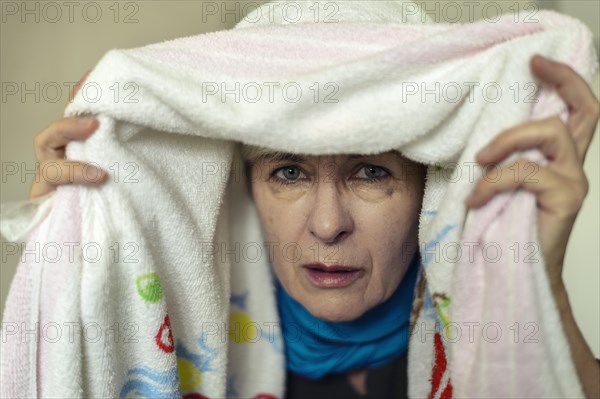 Senior woman with a cold inhaling under a towel