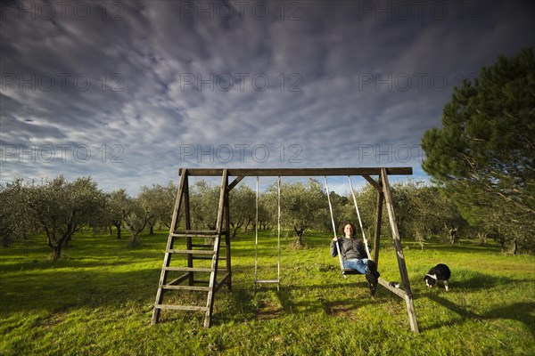 Girl swinging on a wooden swing in front of an olive grove