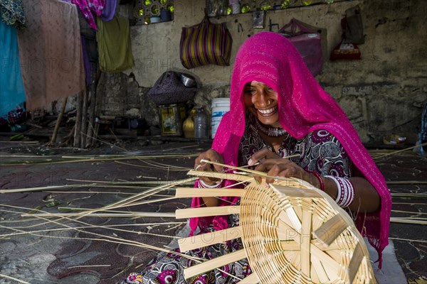 Woman covered in a pink veil is braiding a basket on the pavement