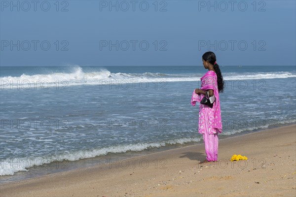 Woman wearing a pink shalwar kameez standing on the beach facing the sea