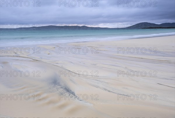 Water flows into the sea at low tide via a sandy beach
