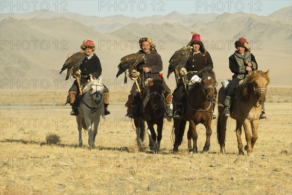 Four Kazakh eagle hunters on their horses on the way to the Eagle Festival in Sagsai