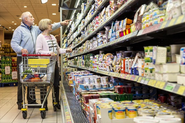 Senior couple shopping with a shopping trolley in the refrigerated dairy section in a supermarket