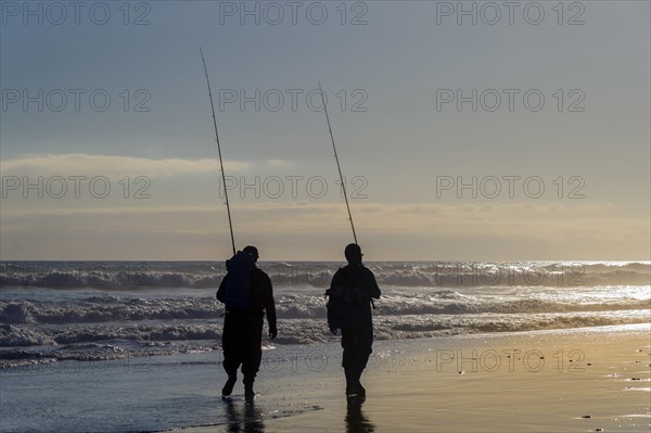 Two anglers walking with their fishing rods along the seaside beach
