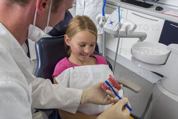 Dentist showing a girl the proper use of a toothbrush