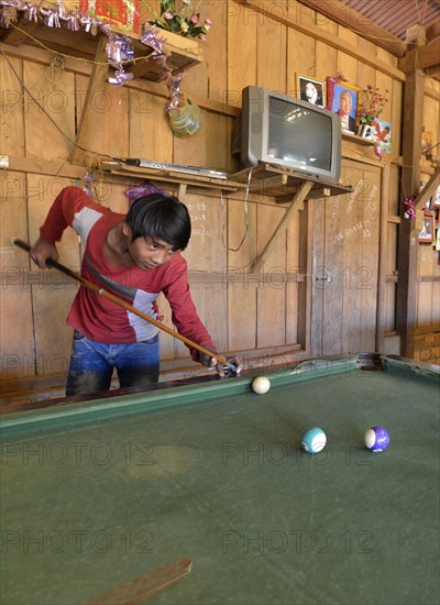 Cambodian youth playing pool billiards in a simple wooden hut