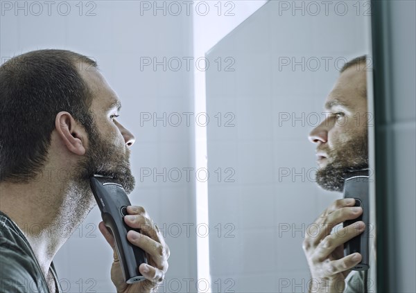 Man shaving his beard in front of a mirror