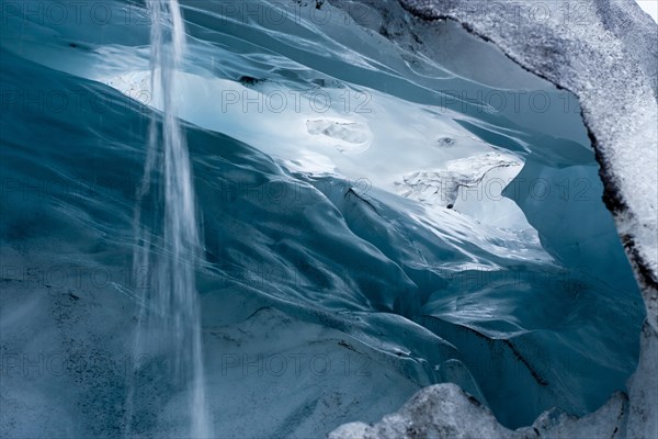 View into a blue-green ice cave with condensation water draining off