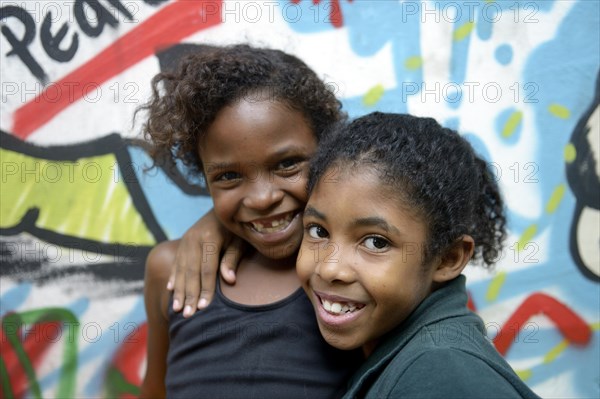 Two smiling girls embracing each other in front of a graffiti-sprayed wall