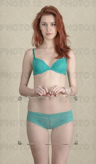 Young woman wearing green lingerie and holding transparent briefcase in front of her