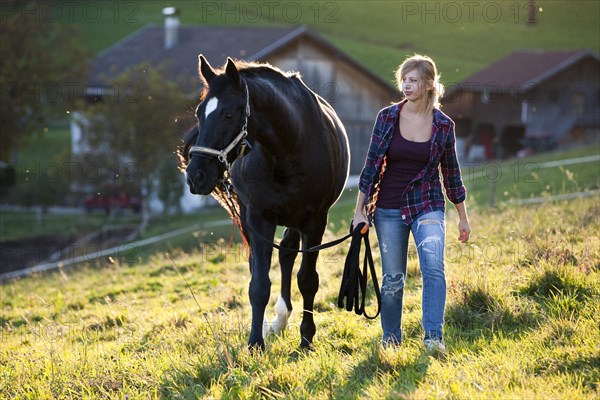 A young woman and a black Hanoverian horse walking on a mountain meadow