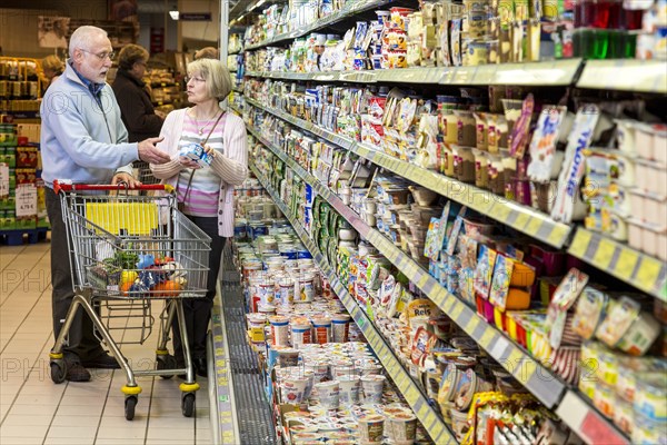 Senior couple shopping with a shopping trolley in the refrigerated dairy section in a supermarket