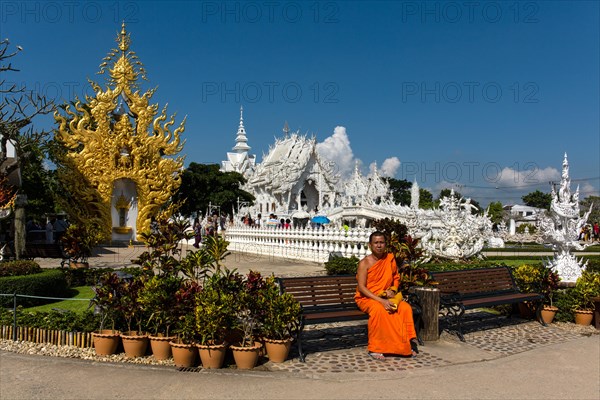 Monk sitting in front of the ornate golden entrance of Wat Rong Khun