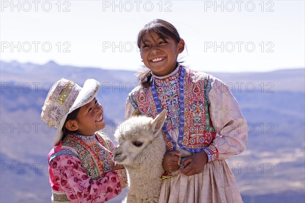 Two girls in traditional dress with an alpaca