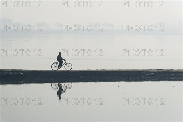 A cyclist crossing the Yamuna river on a dam in the morning haze