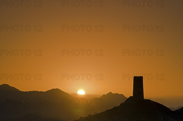 Sunrise behind the silhouette of a lone decaying watch tower at the edge of the Wahiba Sands desert