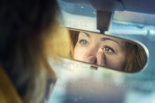 Young woman looking at herself in a rear-view mirror whilst dabbing away tears