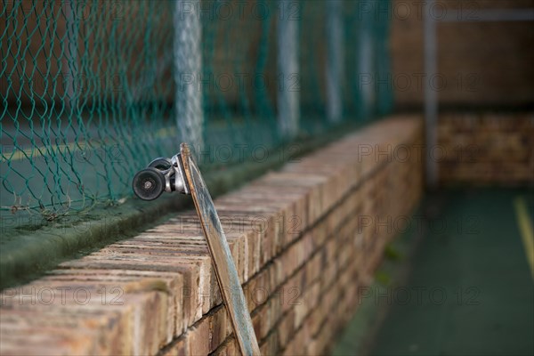 Skateboard leaning against a brick wall in tennis court yard