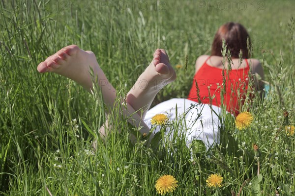 Young barefoot woman lying on her stomach in a flowering spring meadow