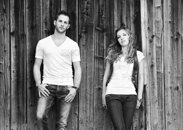 Young man and a young woman leaning against wooden wall