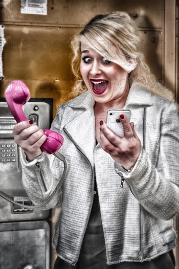 Young woman having to choose between a mobile phone and a phone booth