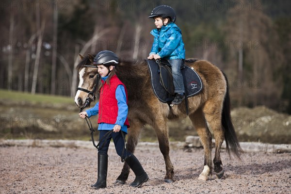 Girl leading a pony with a young child riding it