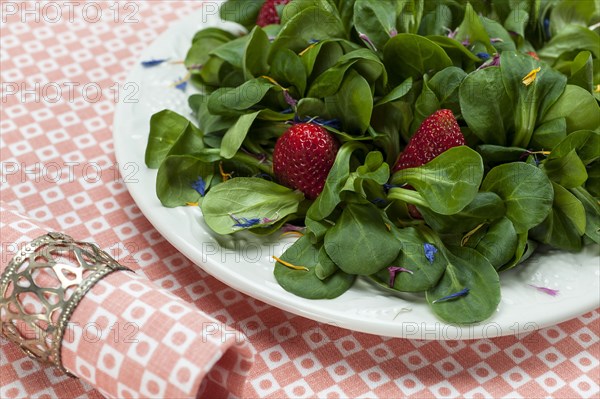 Lamb's lettuce with strawberries and flower petals served on a plate