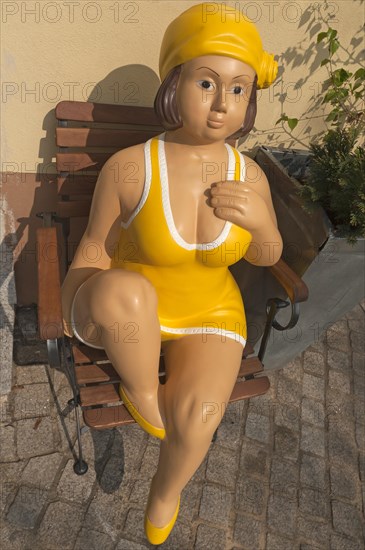 Female figure from the 1950s sitting on a garden chair in front of an ice cream shop