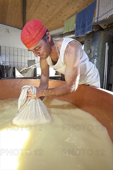 Dairyman drawing cottage cheese with a cloth from the copper kettle for a first test