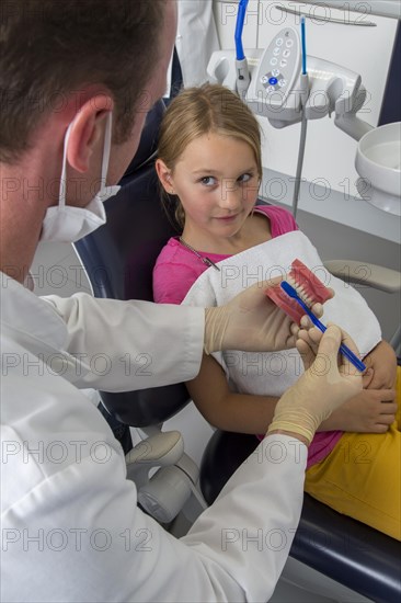 Dentist showing a girl the proper use of a toothbrush