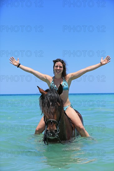 Woman wearing a bikini riding a Barb horse in the sea