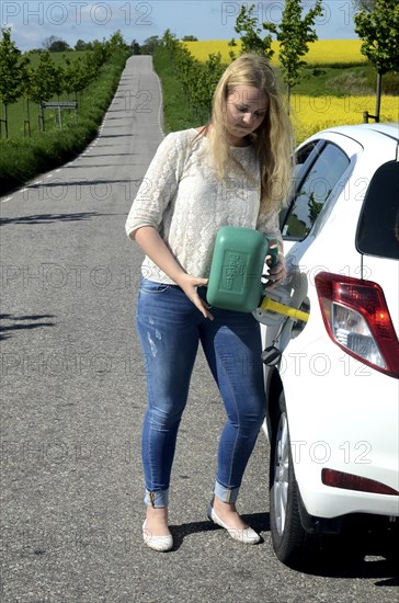 Woman filling petrol into her car from a petrol can