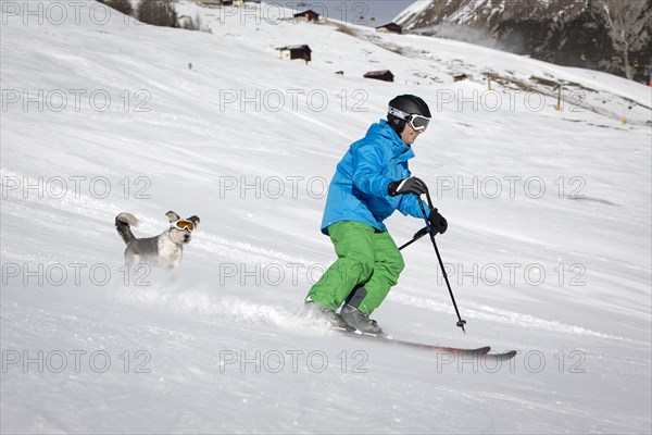 A skier and his dog with snow goggles on a ski slope