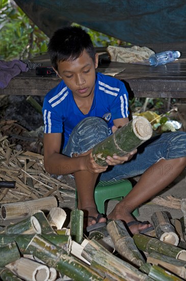 Boy cleaning bamboo tubes used in the preparation of the traditional rice dish Kralan or Khao Lam