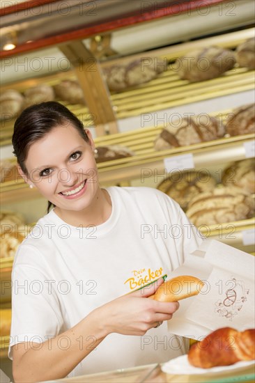 Saleswoman in a bakery packing a bun in a bag